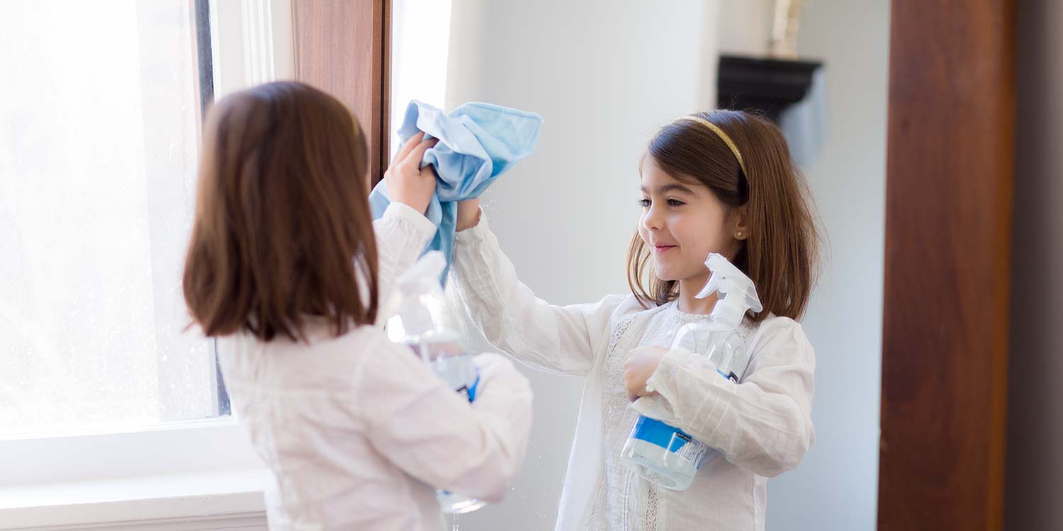 A little girl using Better Life's Glass Cleaner to clean a wall mirror