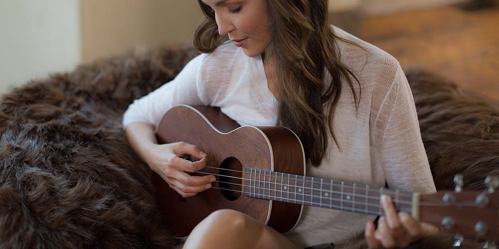An image of a woman sitting comfortably on a furry Comfy Sack while strumming a guitar