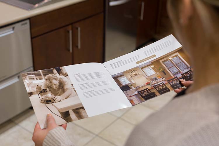 A person looking through a Kirkwood Stair pamphlet showing a person working, some text, and a completed kitchen